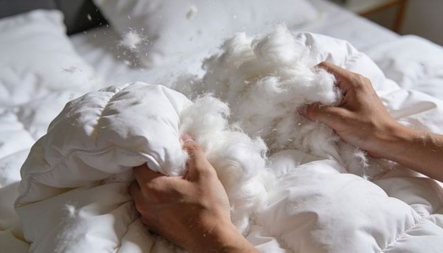 Hands pulling open white comforter releasing fluffy down filling in bright bedroom