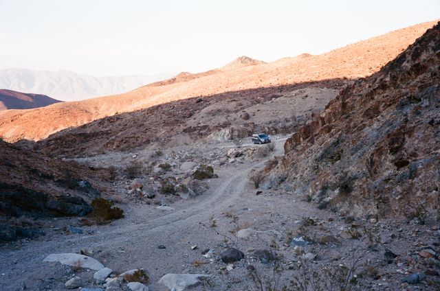 SUV driving along rugged, rocky path in desert mountain region. Rugged terrain, suitable for discussing off-road vehicles, adventure tourism, and remote exploration. Highlights beauty and challenge of pioneering paths, ideal for travel blogs, automotive promotions, and outdoor adventure content.