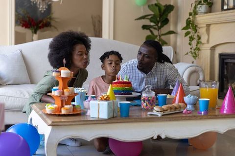 African american family celebrating child birthday at home blowing out rainbow cake