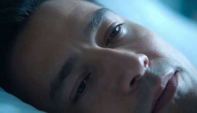 Lying adult man showing fine skin lines on pale blue pillow closeup, calm cool lighting