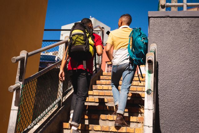 Two young men with backpacks are walking up a set of stairs on a sunny day. This image can be used for themes related to travel, adventure, friendship, and urban exploration. It is ideal for promoting tourism, city breaks, and backpacking holidays.