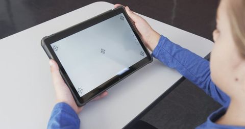 Child holding tablet with calibration markers and glare while sitting at classroom desk