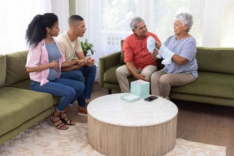 Grandparents presenting baby onesie to expectant couple in multigenerational living room