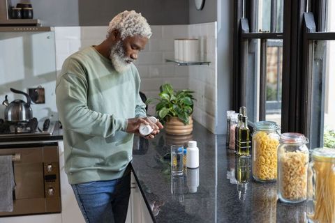 Senior african american man reading prescription bottle on kitchen counter at home