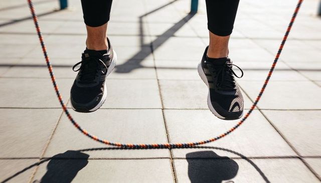 Skipping rope mid-jump casting braided rope shadows on sunlit urban pavement for workout