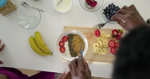 African american couple assembling healthy yogurt bowl with fruit, granola and teamwork