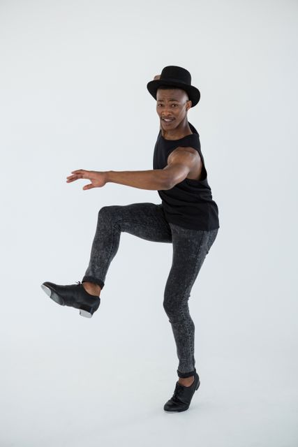 Male dancer in black outfit performing energetic dance moves against white background. Suitable for use in articles about dance, fitness, performing arts education, and creative expression. Can be used in promotional materials for dance studios or fitness programs. Ideal for illustrating themes of movement, discipline, and artistic practice.