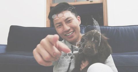 Smiling man holding dog pointing with hexagon tech overlay on modern living room couch