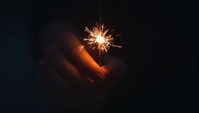 Closeup Hand Holding Lit Sparkler at Night with Bright Sparks and Warm Ambient Glow