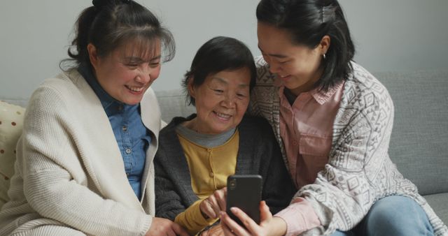 Smiling senior asian woman using smartphone with adult daughter and granddaughter embracing - Download Free Stock Photos Pikwizard.com
