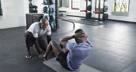 Trainer Assisting Client with Sit-Ups in Modern Gym Environment
