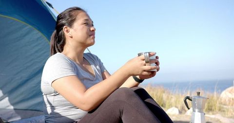 Woman relaxing with drink outside tent during mountain camping