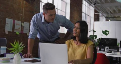 Colleagues collaborating over laptop in modern industrial loft office with greenery