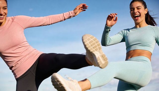 Energetic women kicking in colorful activewear outdoors under bright blue sky