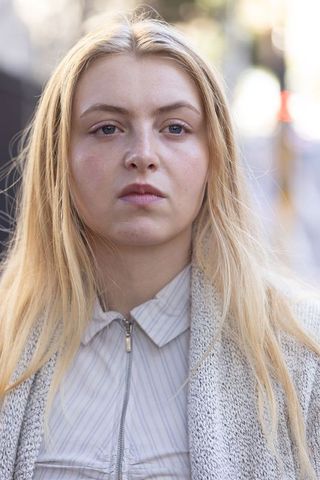Young blonde woman looking ahead on urban street portrait with calm expression and bokeh