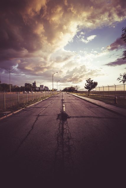 Image depicts a deserted city street at sunset with dramatic clouds overhead. Ideal for themes related to urban exploration, solitude, peacefulness, travel, and dramatic skies. Perfect for use in travel brochures, blog articles about urban scenery, or inspirational posters emphasizing quieter moments in city life.