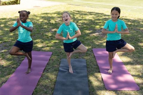 Diverse school girls practicing yoga tree pose on grassy field showcasing balance teamwork