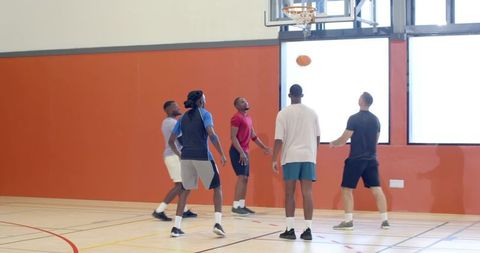Men playing indoor basketball reaching for rebound near hoop in community gym