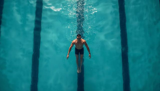 Top-down male swimmer gliding down pool lane cutting wake and creating ripples