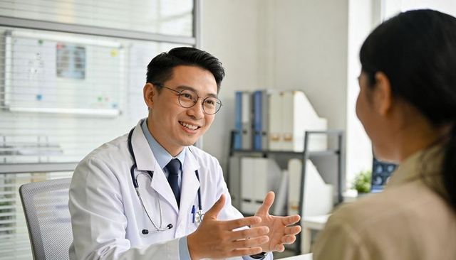 Smiling male doctor consulting patient and gesturing with hands in modern medical office