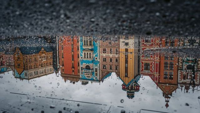 Reflecting puddle capturing colorful historic facades on wet urban street with raindrops
