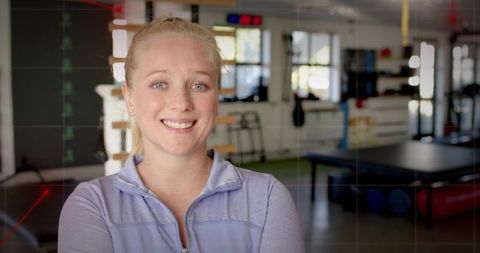 Smiling physical therapist wearing light purple jacket facing camera in rehab studio