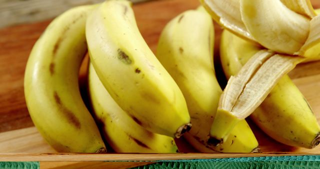 A bunch of ripe bananas sits on a wooden surface, with one partially peeled, revealing the soft fruit inside. Bananas are a popular fruit known for their potassium content and sweet taste.