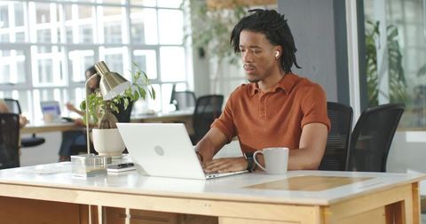 African American man working on laptop in bright open-plan coworking space with plants