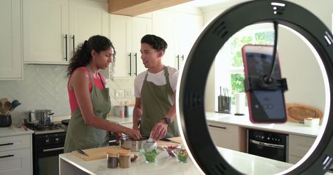 African American couple filming cooking tutorial on kitchen island with ring light