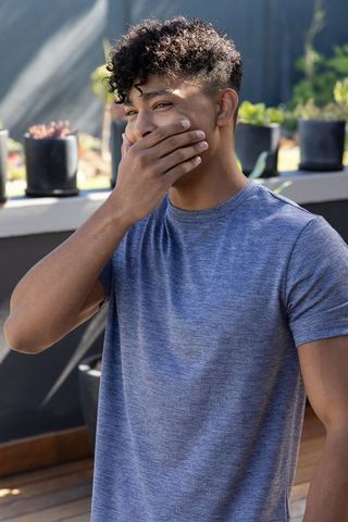 African american man covering mouth while laughing on rooftop deck with succulents