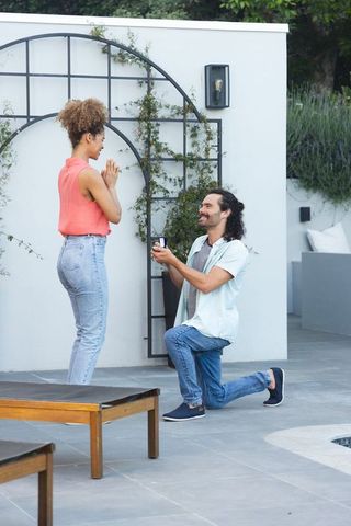 Kneeling man proposing to partner on private patio by pool, outdoor engagement