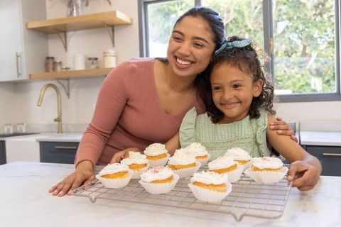 Smiling mother and daughter baking and decorating cupcakes in bright modern kitchen