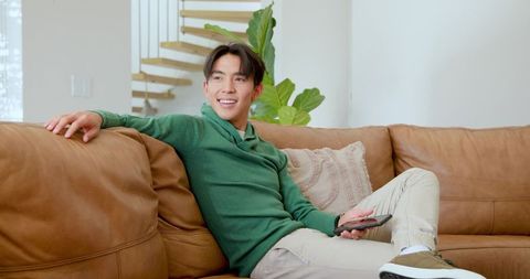 Young man relaxing on sofa holding remote in modern living room