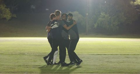 Night cricket team celebrating victory under floodlights on grass field