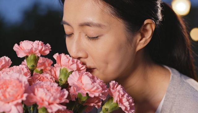 Asian woman inhaling bouquet of pink carnations on patio at dusk, serene closeup portrait