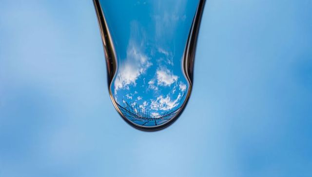 Elongated Water Droplet Reflecting Blue Sky and Railing, Lenslike Inverted View