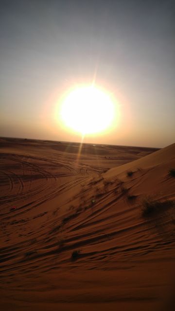 Beautiful shot of the sun setting over expansive sand dunes in a desert. The warm, golden hues of the sunset and the soft contours of the sand create a serene and tranquil atmosphere. Useful for travel brochures, nature blogs, backgrounds, and inspirational content emphasizing nature's beauty and peaceful moments.