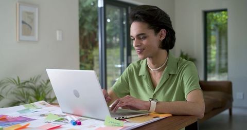 Young professional working remotely typing on laptop at home desk with colorful sticky notes