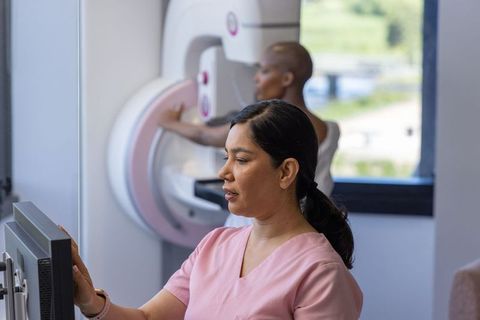 Female radiology technician operating mammography console while patient positioning