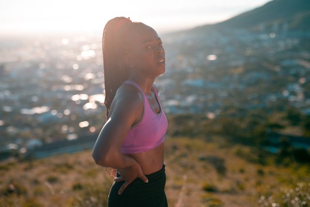 This image showcases a fit African American woman engaged in physical exercise in a scenic countryside area during sunset. Ideal for use in advertising campaigns emphasizing outdoor fitness, health and wellness, and active lifestyles. Perfect for websites, blogs, and social media posts promoting running, exercise routines, and healthy living in natural settings.