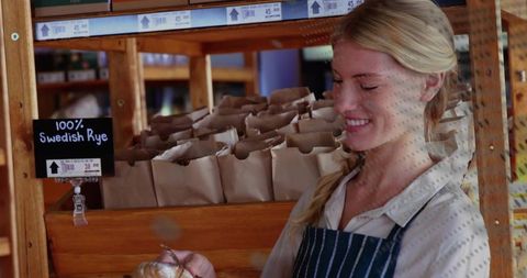 Smiling baker holding freshly baked roll beside wooden 100% Swedish Rye display