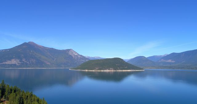 A serene lake with a forested island in the center, under a clear blue sky - Download Free Stock Photos Pikwizard.com
