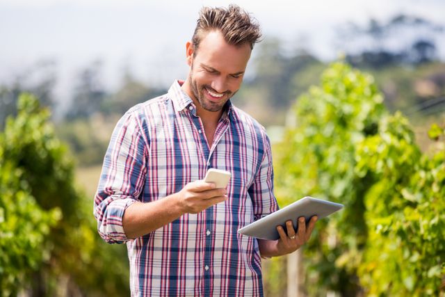 Young man with digital tablet using mobile phone at vineyard on sunny day