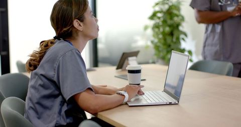 African American Nurse in Gray Scrubs Working on Laptop During Healthcare Team Meeting