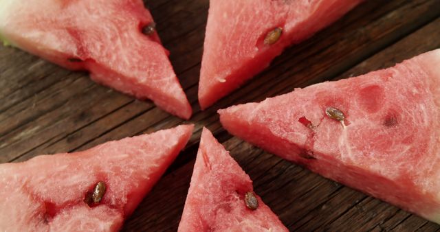 Slices of fresh watermelon arranged in a circular pattern on a rustic wooden table. Ideal for summer-themed projects, healthy eating content, recipes, or fruit promotion. This image captures the essence of summer fruits with its vibrant red color and visible seeds, perfect for use in food blogs, advertisements, or social media posts promoting fresh produce.