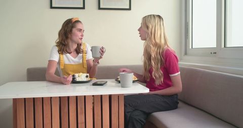 Friends sharing cake and coffee in bright kitchen nook, chatting over dessert and mugs