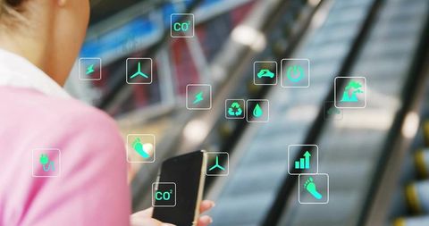 Woman holding smartphone on escalator viewing AR eco icons for smart commuting solutions