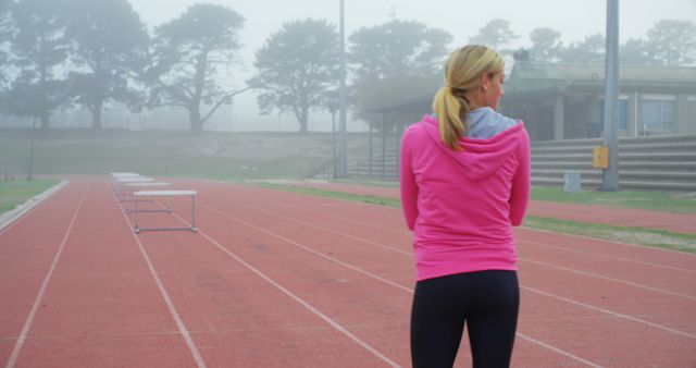 Female athlete in pink hoodie preparing for track workout on foggy morning - Download Free Stock Images Pikwizard.com