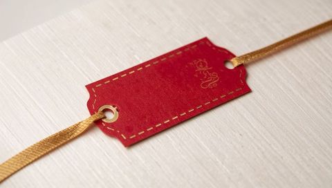 Crimson gift tag with gold stitch border and metallic ribbon on pale wood board