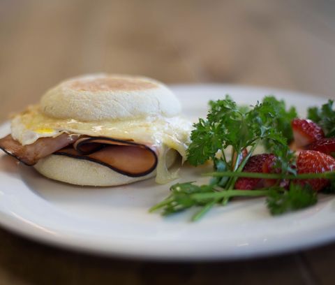 Breakfast sandwich with melting cheese on English muffin, ham and fresh strawberries